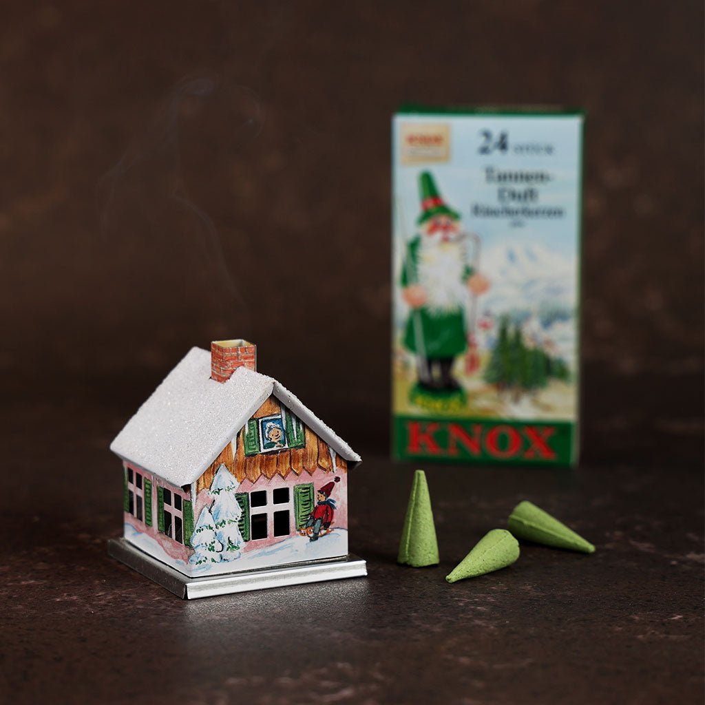 Small metal incense smoker cottage house in front of incense cones and box on dark background