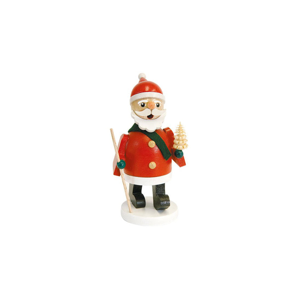 A small Santa Claus incense burner standing on a white base, wearing a red coat and hat with white trim, a dark green scarf, black boots, and holding a small tree and staff, photographed on a plain white background.