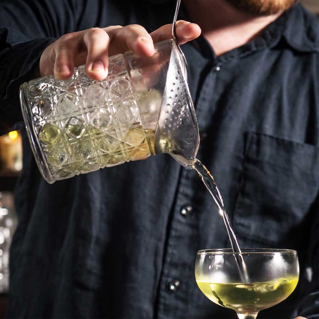 Person pouring a drink from a glass into a wine glass.