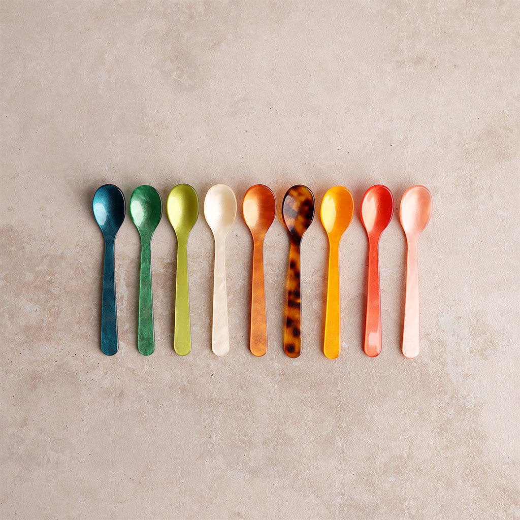 Row of colorful spoons on a beige background