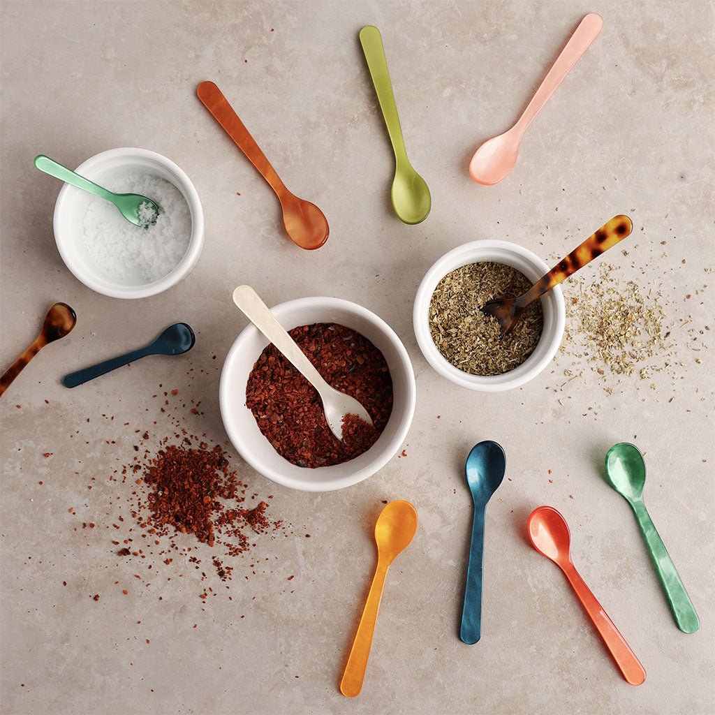 Colorful spoons and bowls with various spices on a textured surface