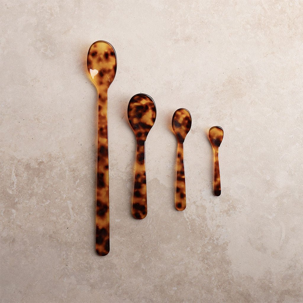 Set of four tortoiseshell spoons on a textured beige surface