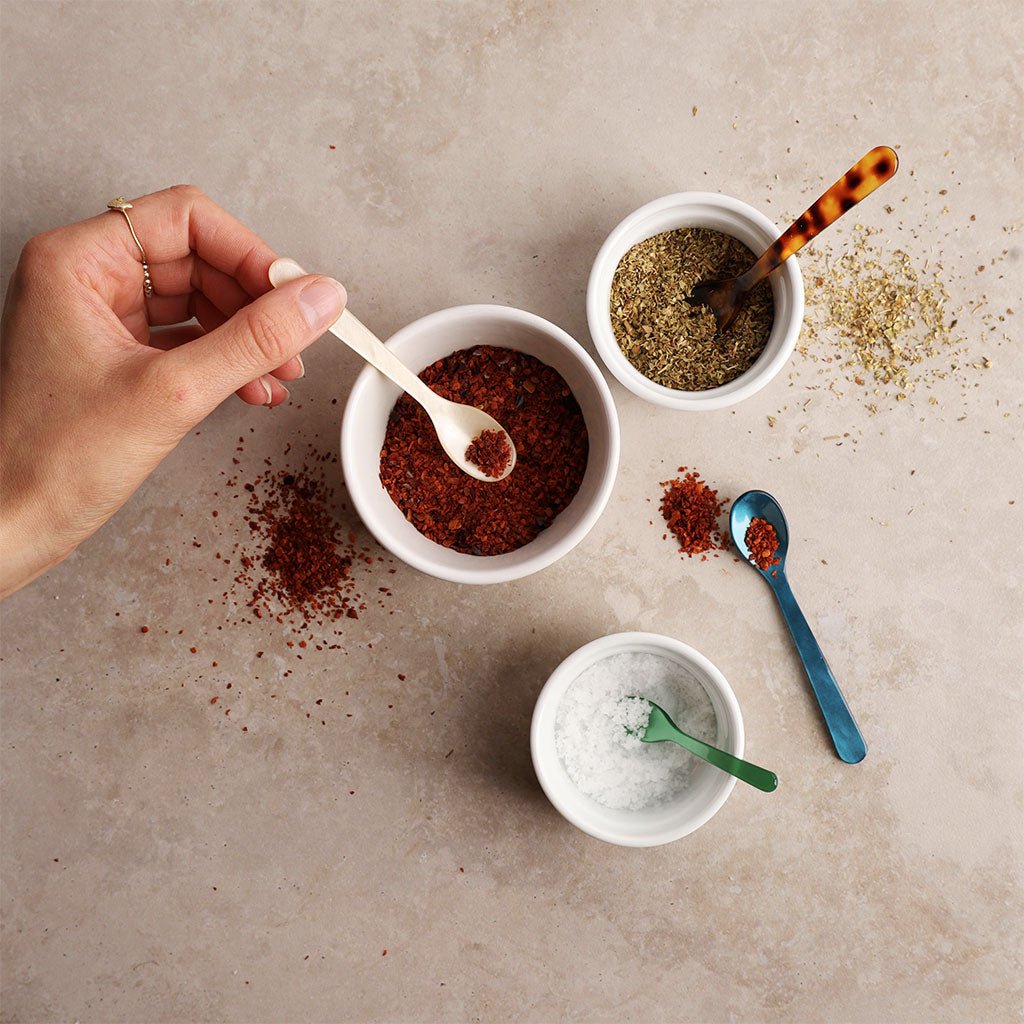 Hand holding a spoon over a bowl of spices on a textured surface