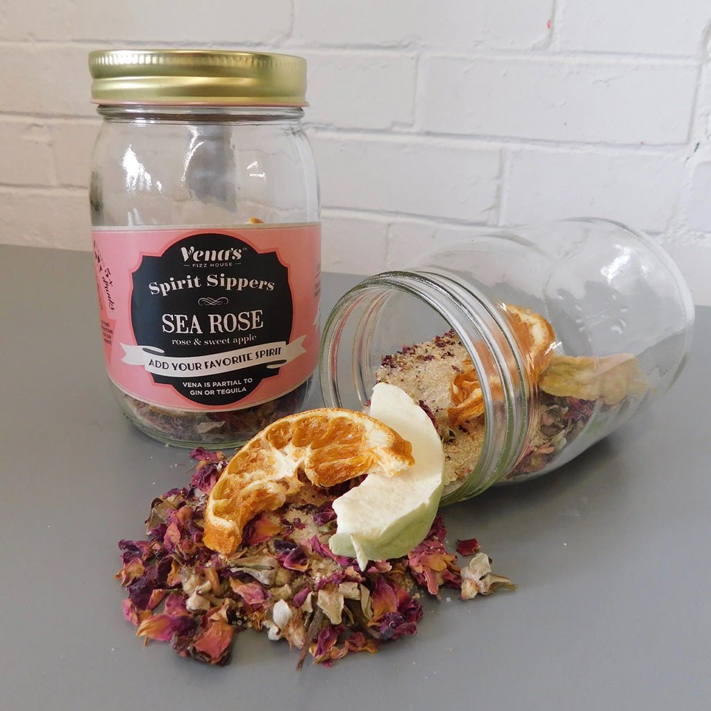 Glass jar with dried herbs and fruits, labeled 'Vena's Spirit Sippers Sea Rose', on a gray surface.