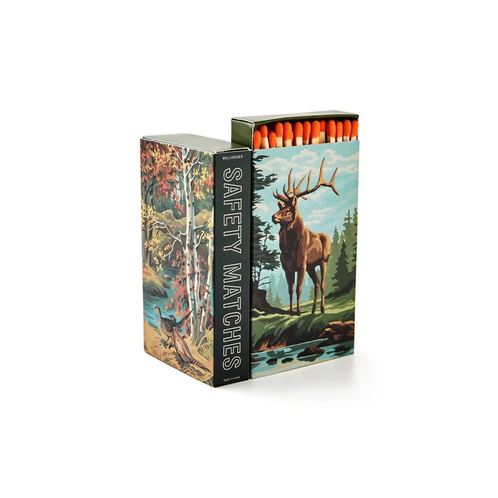 A box of safety matches with a forest illustration featuring a deer and birch trees. The box is open, showing orange tips of the matches, and the words 'SAFETY MATCHES' are printed vertically on the side.
