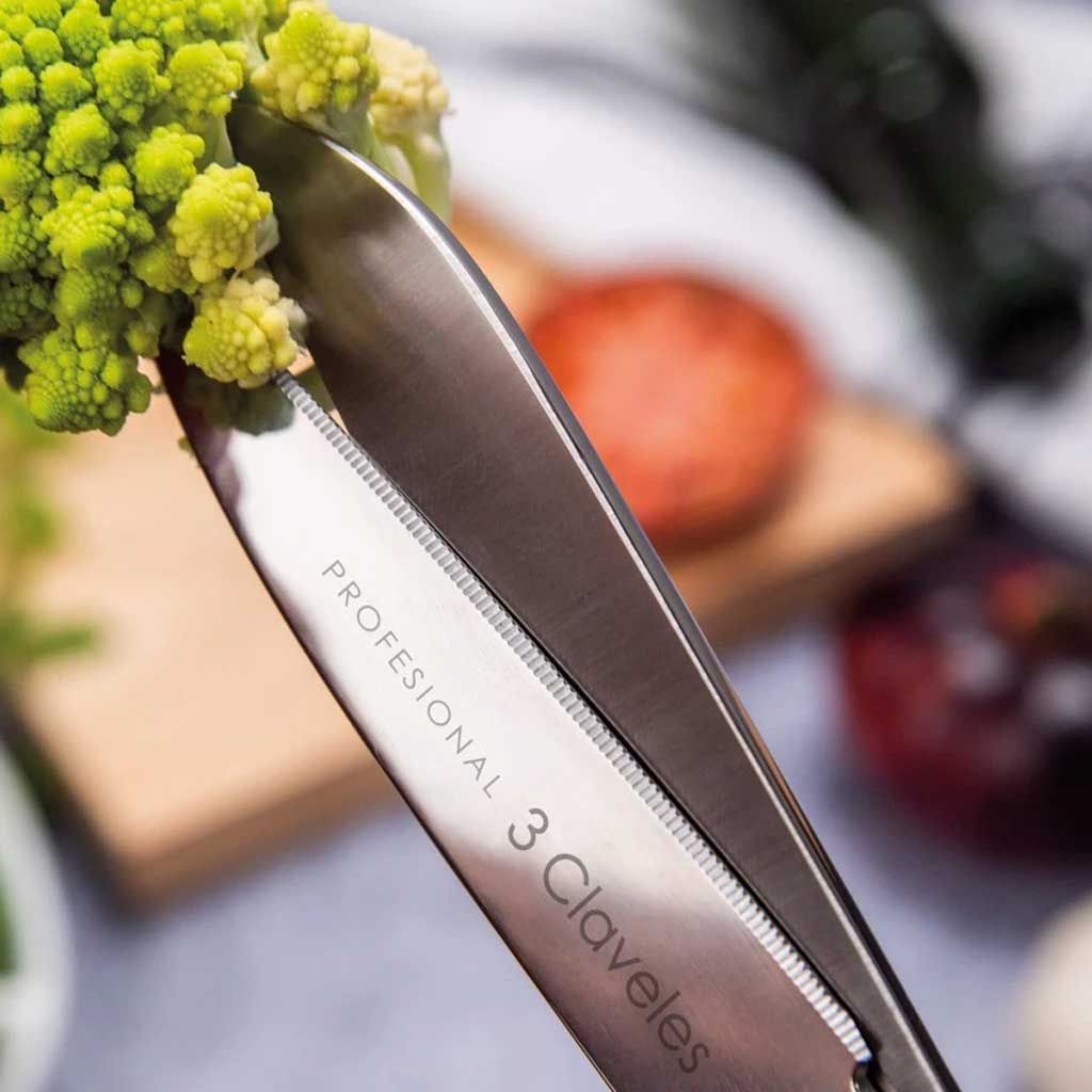 Knife with '3 Claveles' branding holding green vegetable against a blurred kitchen background.