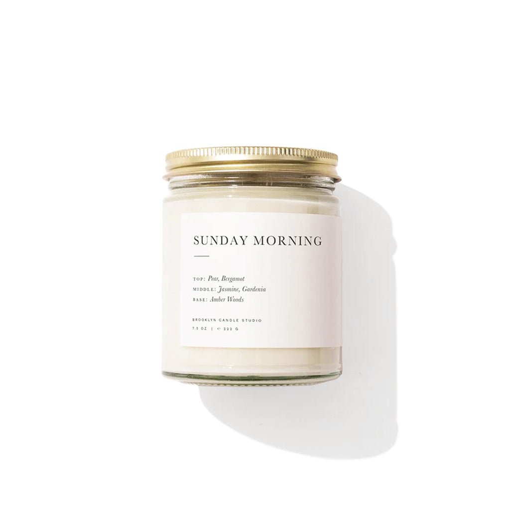 Candle with a gold lid labeled 'Sunday Morning' on a white background