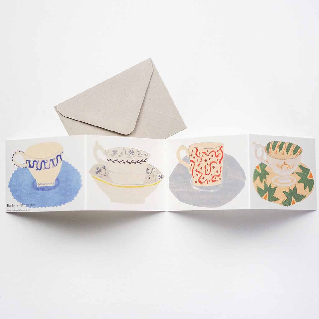 Card opened with teacup and saucer illustrations and a beige envelope on a white background