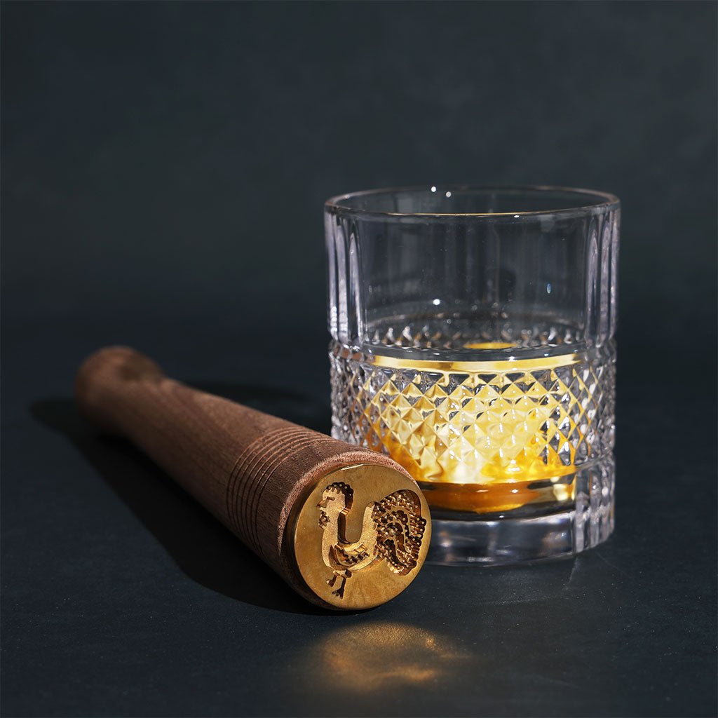 Clear glass with diamond pattern and wooden muddler on a dark background