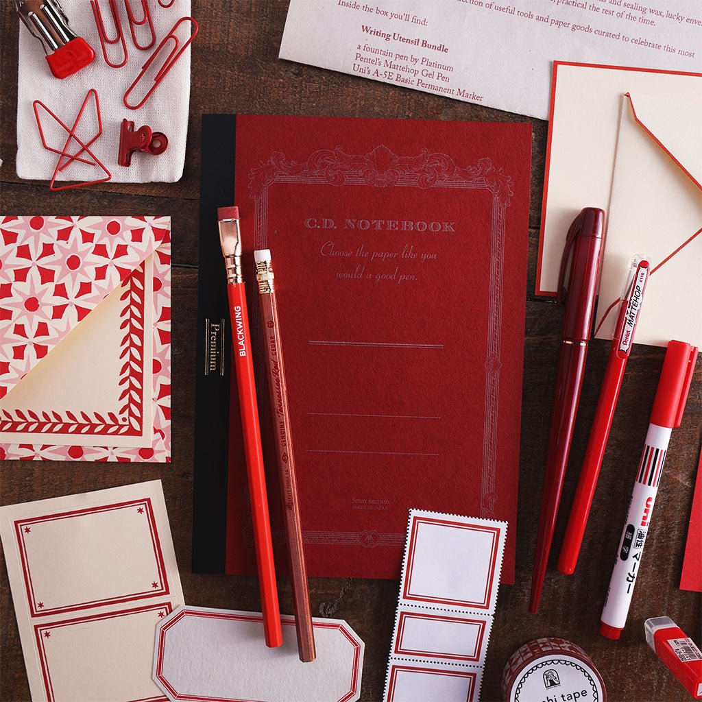 Red-themed office supplies, notebooks, pens, and envelopes.