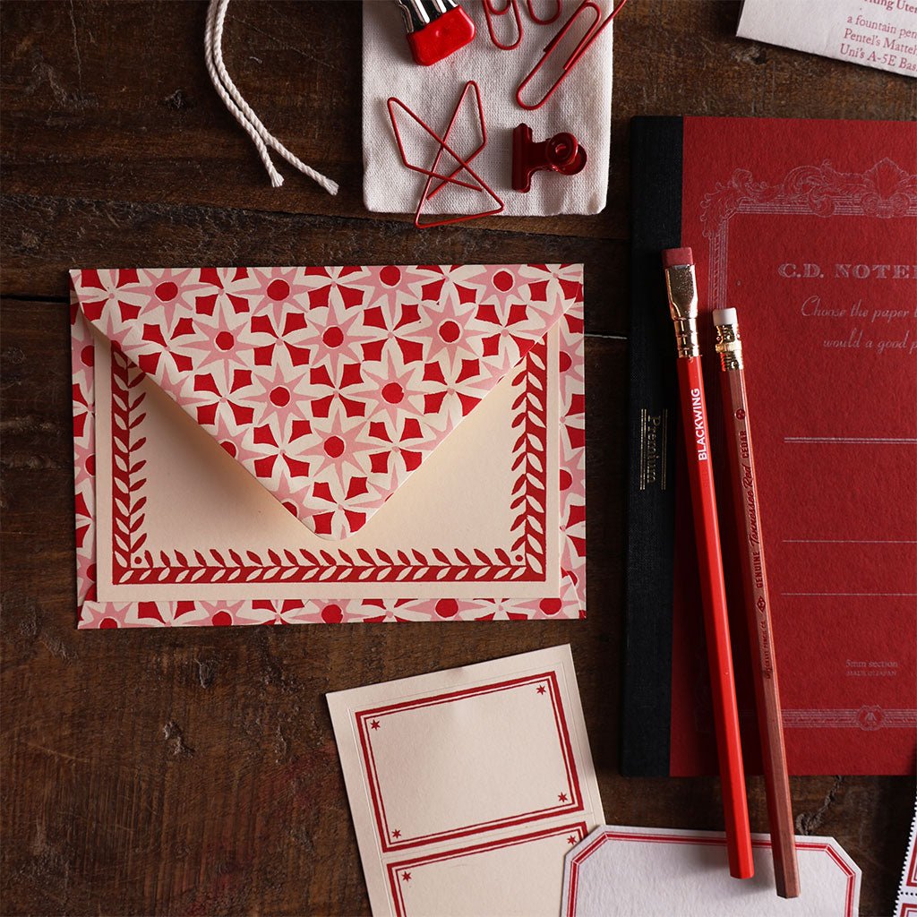 Red notebook, pencils, patterned stationery, and clips.