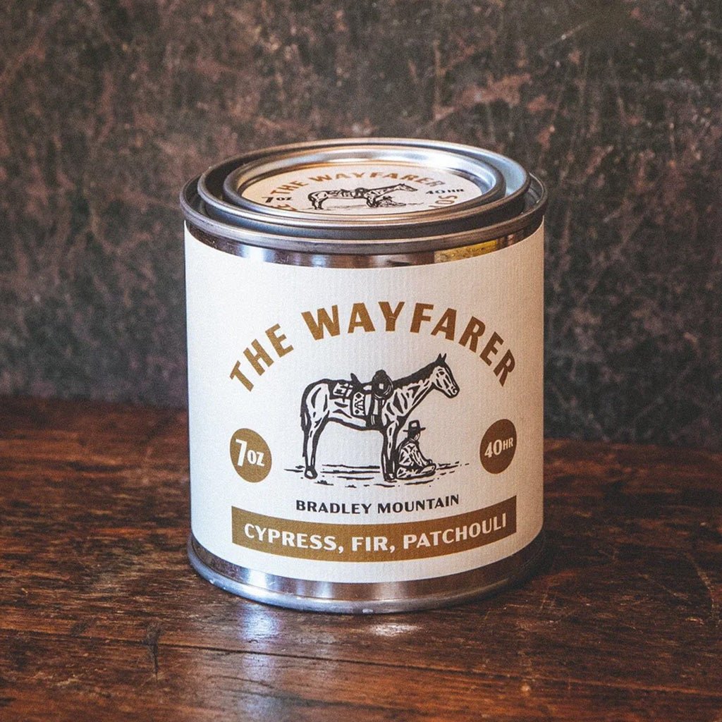 Candle tin labeled 'The Wayfarer' on a wooden surface with a dark textured background