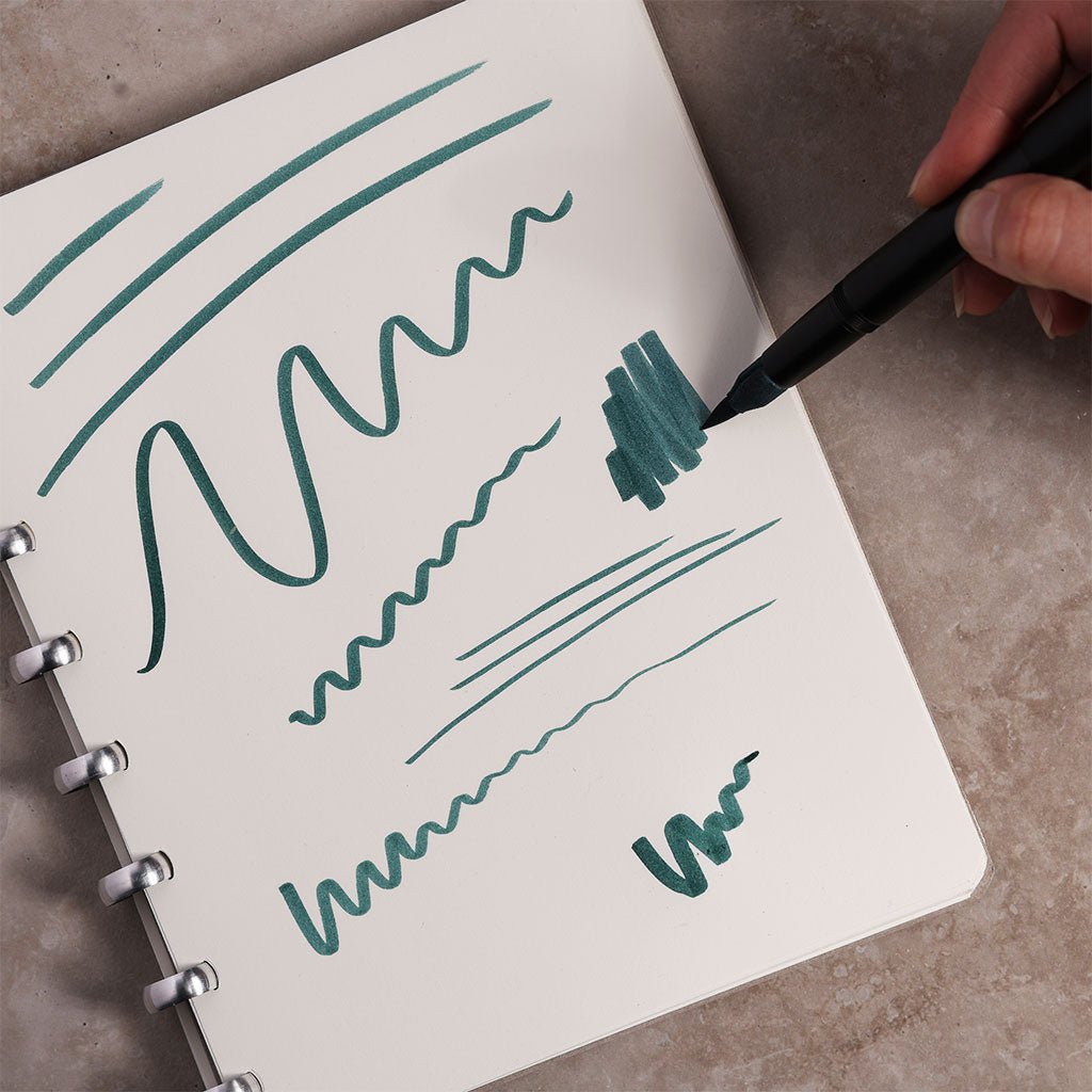 Person writing in a notebook with a green pen on a concrete surface