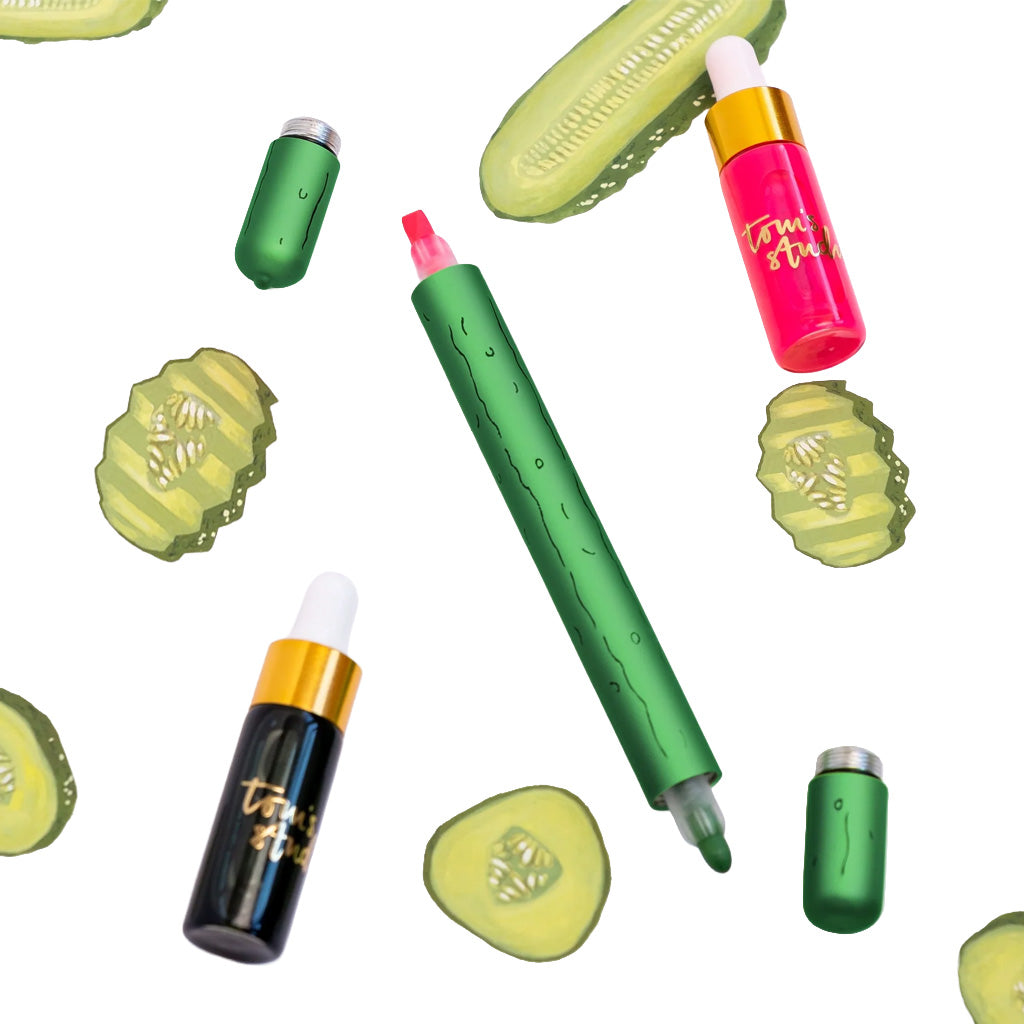 A green dual-sided pen with a pickle design next to bottles of ink and two green caps on white background with floating pickle designs