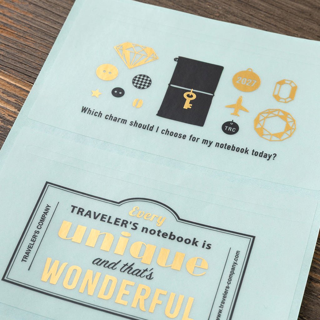 A mint green sheet with gold and black Traveler's Company stickers against wooden surface.