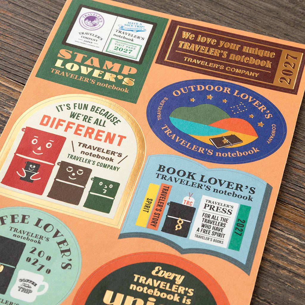 A close-up of a colorful Traveler's Notebook sticker set laid on a wooden surface.