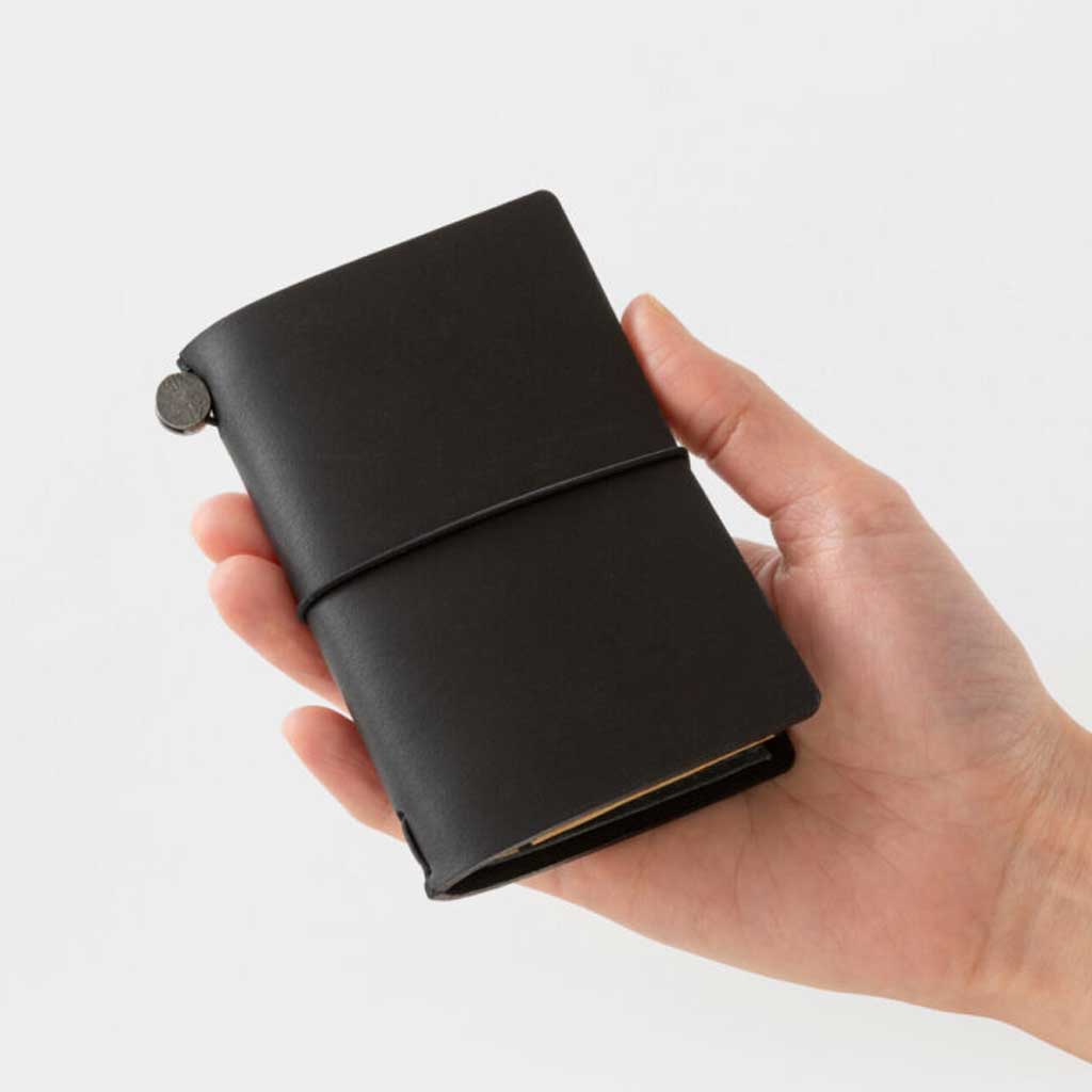Hand holding black card-size notebook against light background