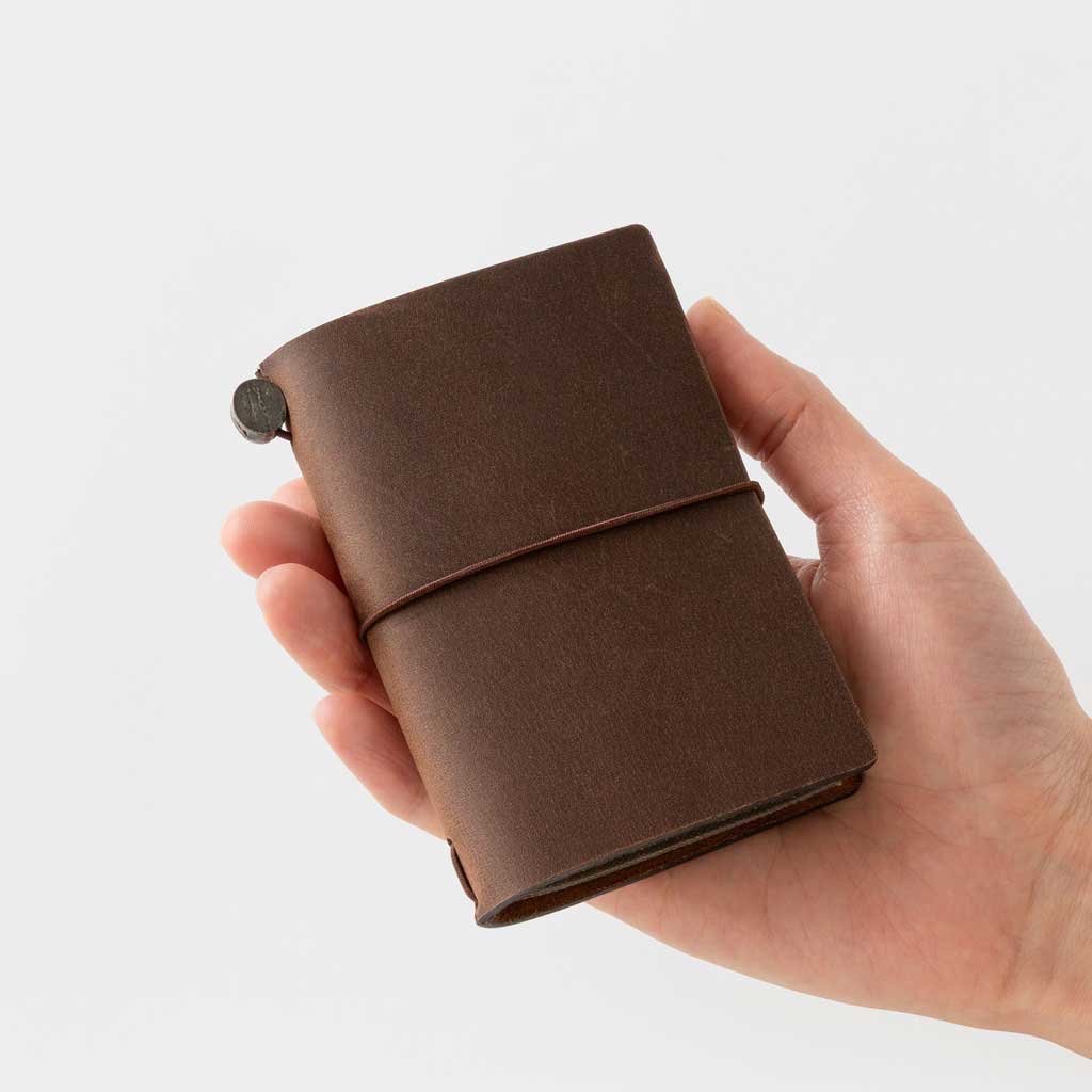 Hand holding brown card-size notebook against light background