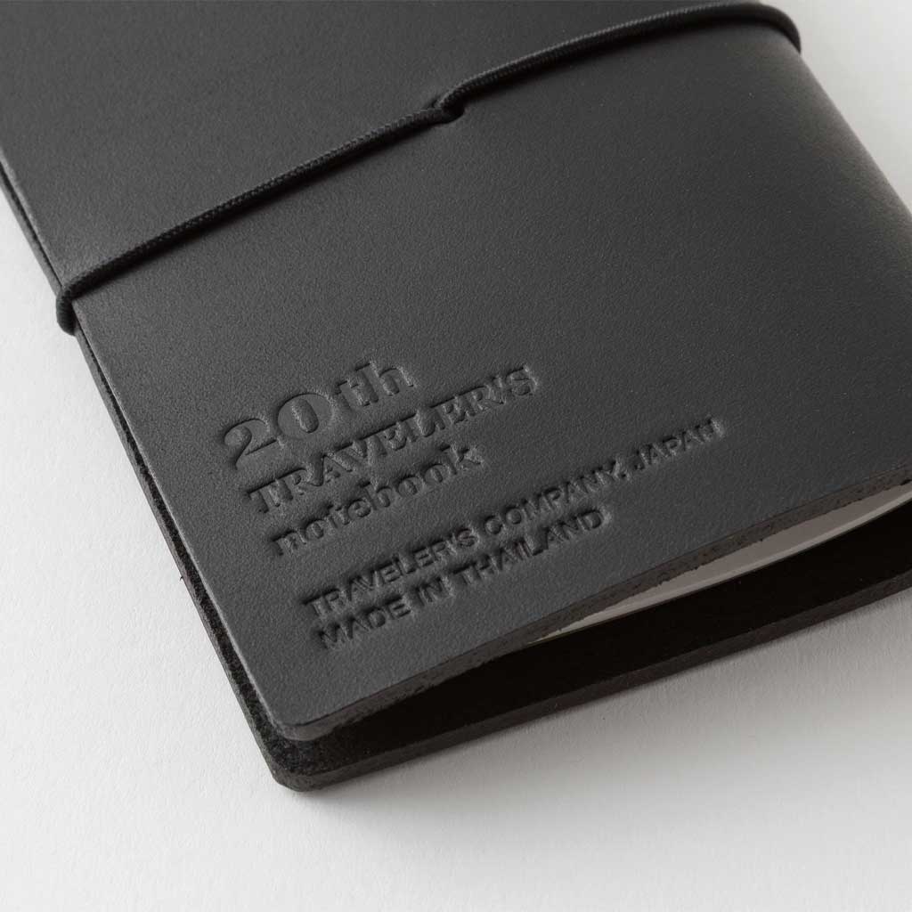 Black leather notebook cover with embossed text that reads "20th traveler's notebook" on a white background