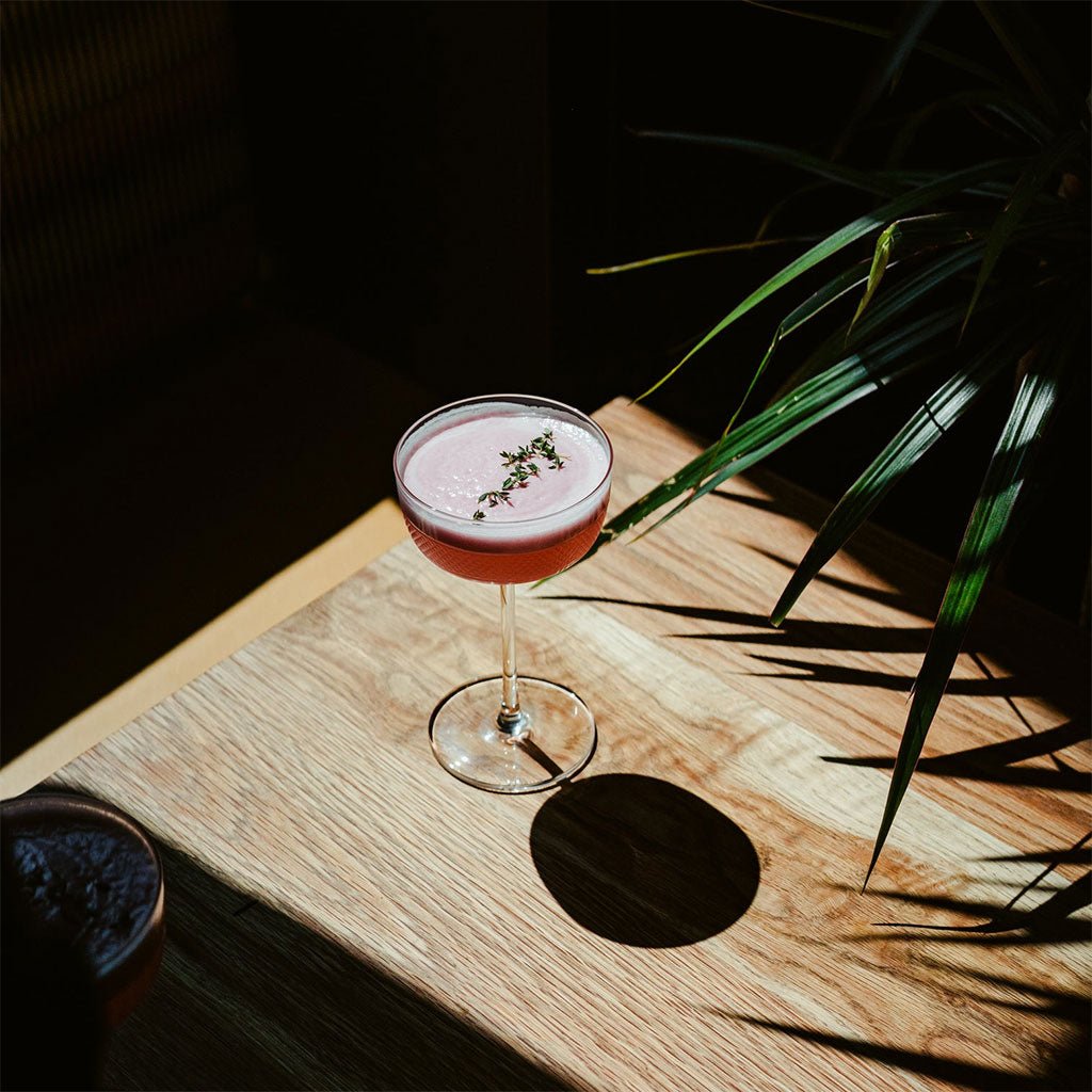 Cocktail in a glass with a dark background and plant shadows