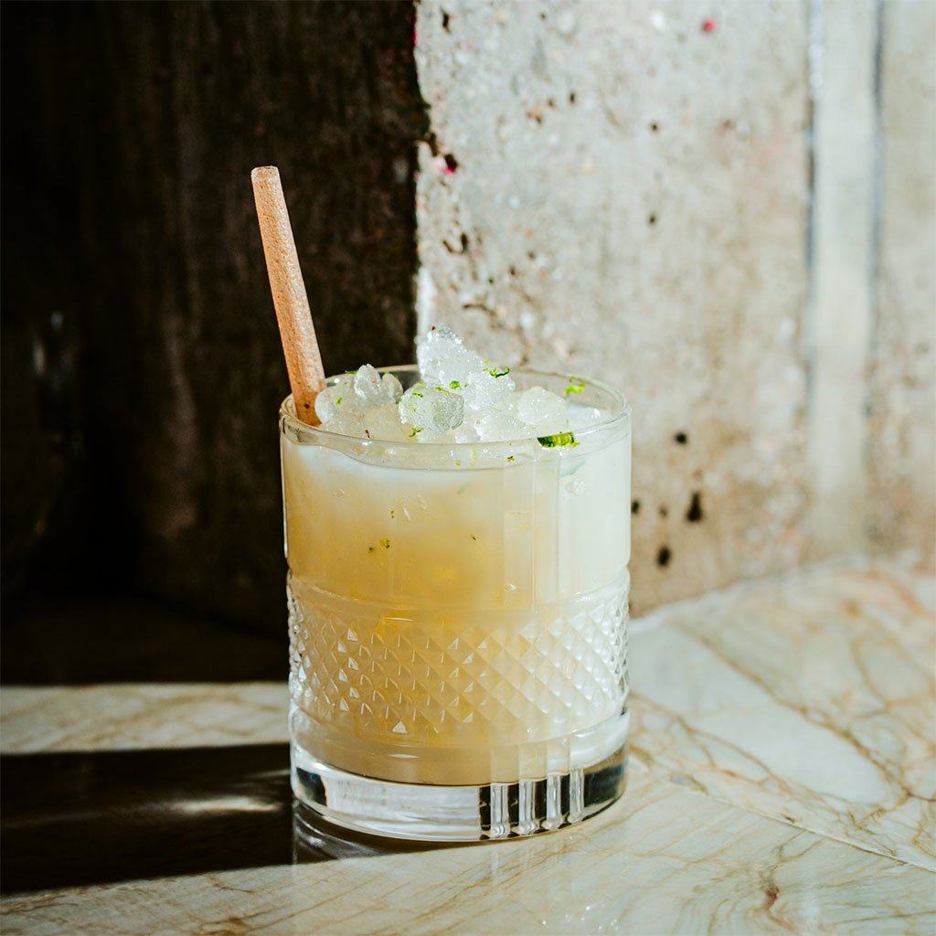 Cocktail with a stirrer in a textured old fashioned glass on a marble surface