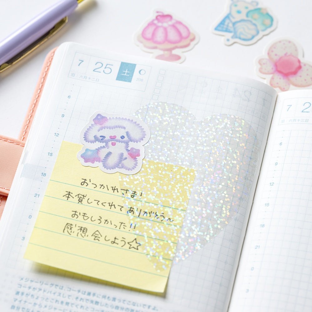 Hobonichi planner page with a sticky note and decorative glittery and pastel stickers on a white surface