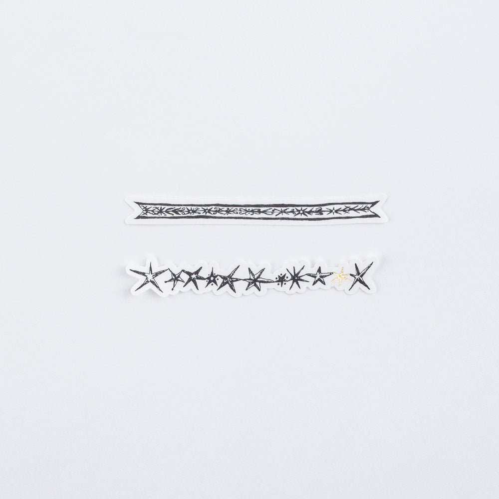 Two decorative black and white stickers with stars and gold accents laying on white surface