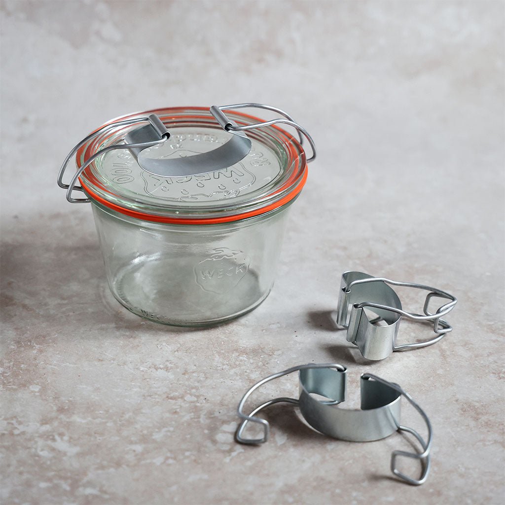 Glass jar with metal lid and two metal clips on a concrete surface