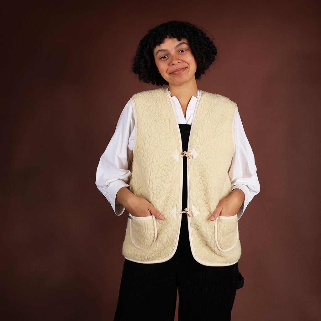 A model wearing a natural woolen vest over a white shirt and black jumper.