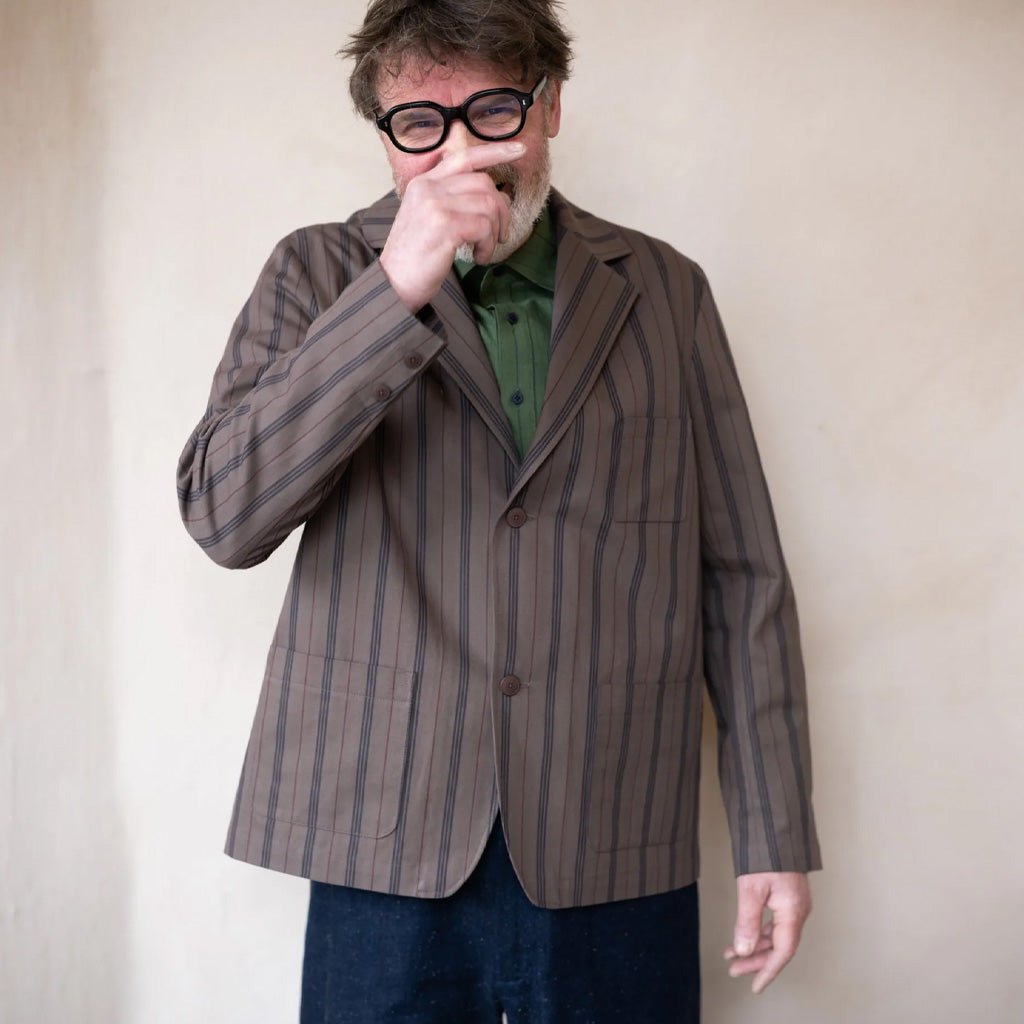 Man wearing a striped brown jacket and glasses, standing against a plain background