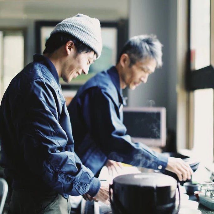 Two men working together at a desk with electronic equipment and tea.