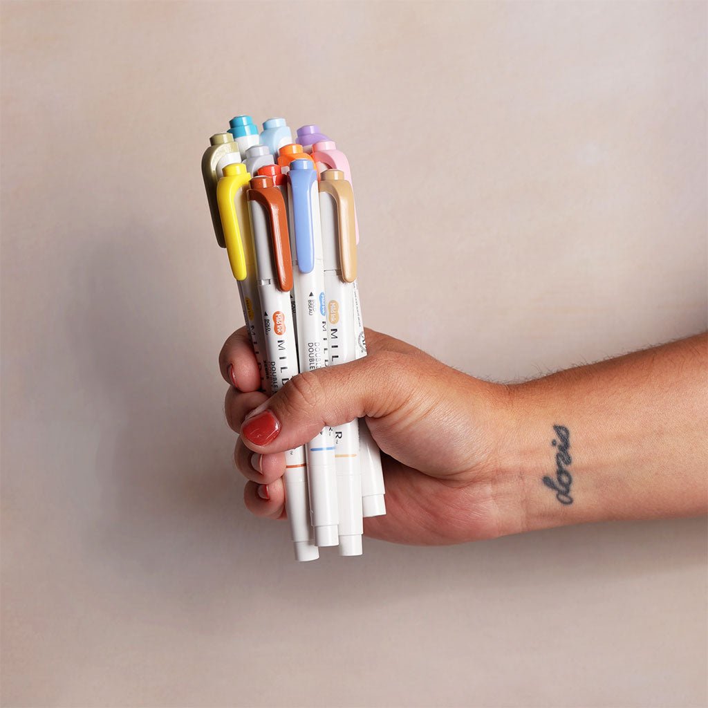 Hand holding a collection of colorful markers against a plain background