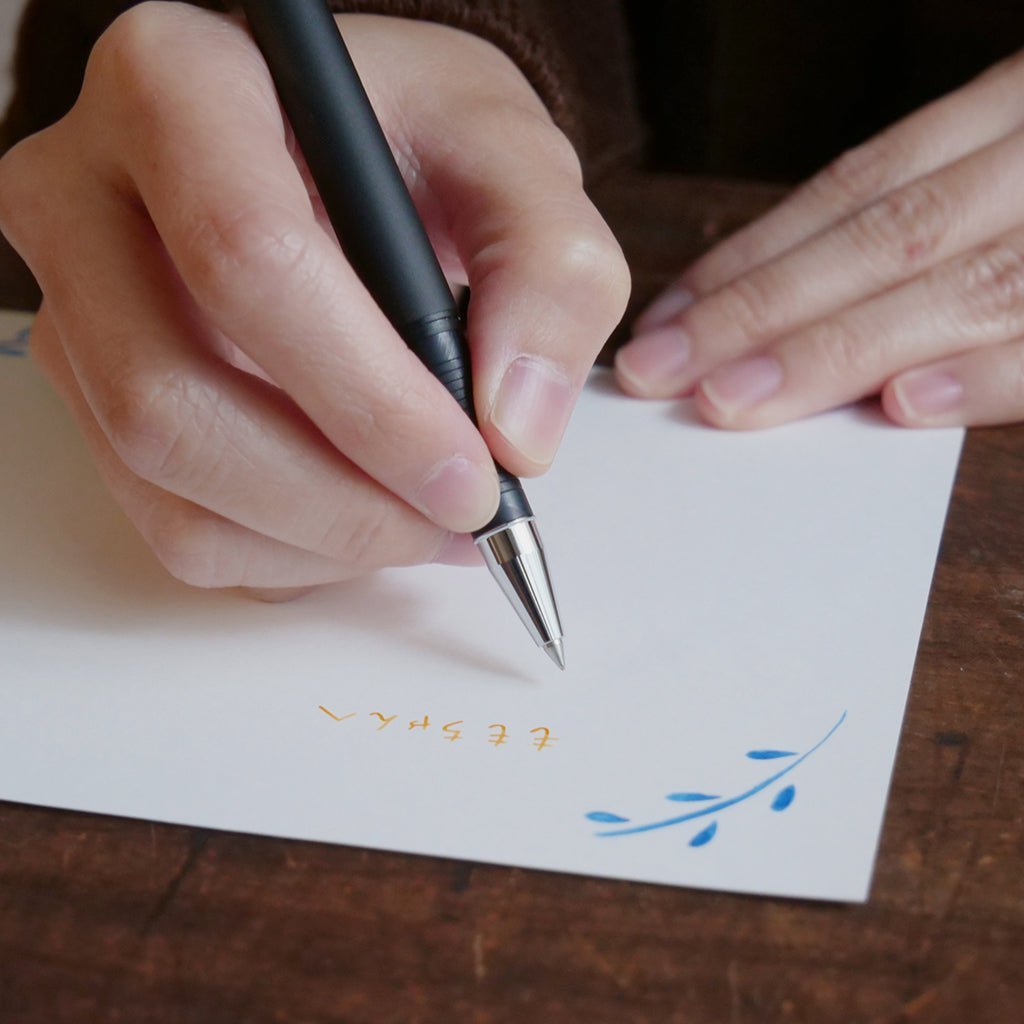 Person writing on a card with a pen against wooden surface.
