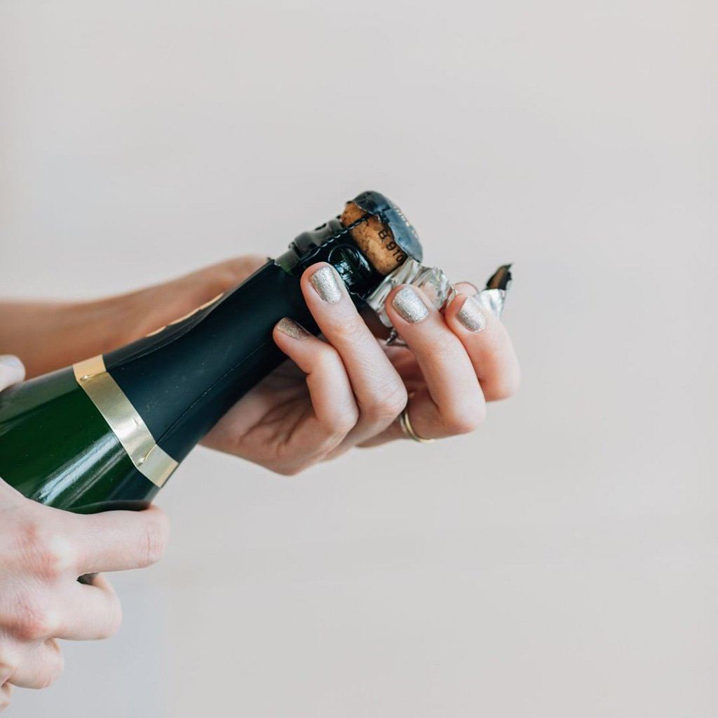 Hand opening bottle of champagne wearing glittery nail polish