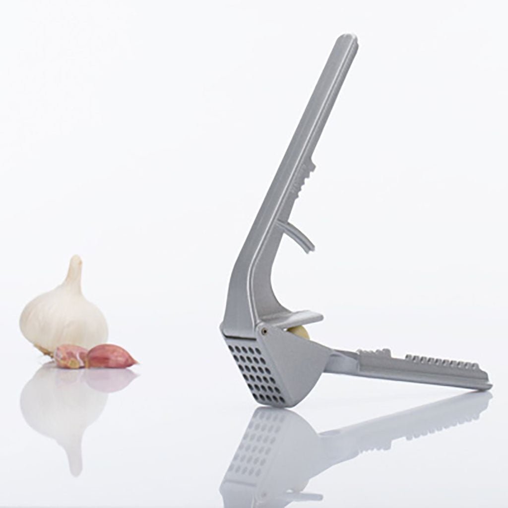 Gray garlic press with a whole garlic bulb and crushed garlic on a white background