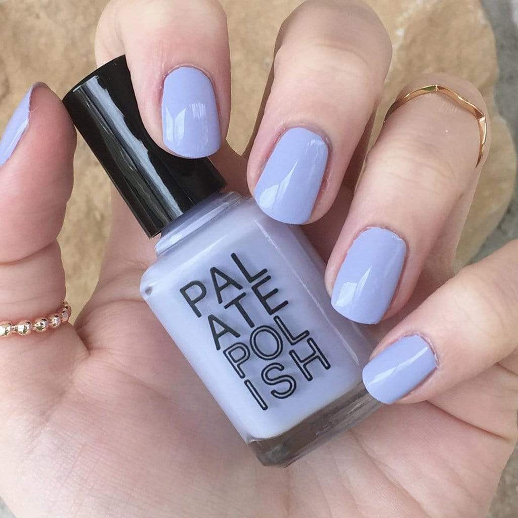 Hand holding a bottle of 'Palate Polish' with light purple nail polish on nails.