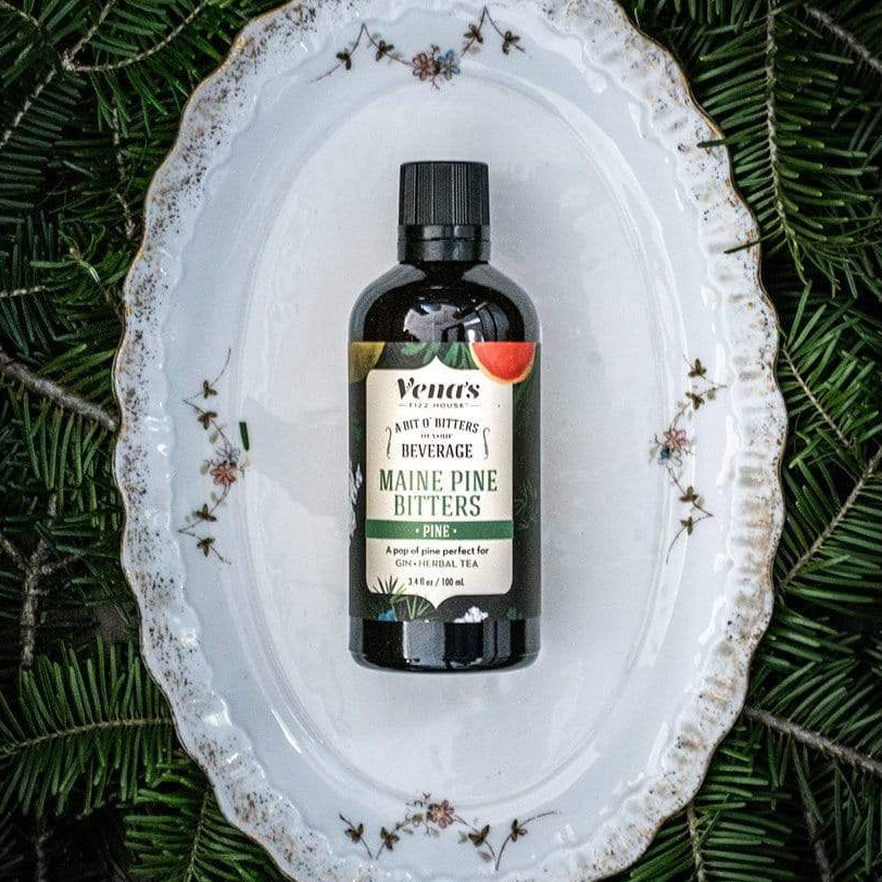 Bottle of Maine Pine Bitters on a decorative white plate with greenery in the background