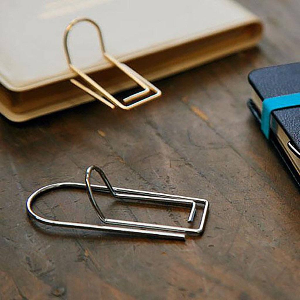 Two metal pen clips on a wooden surface with a notebook in the background.