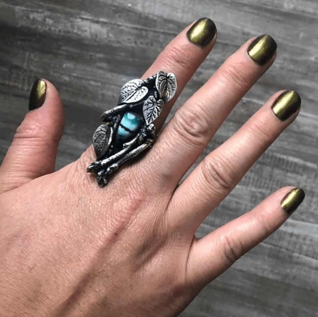 Hand wearing dark shimmery green nail polish against gray background