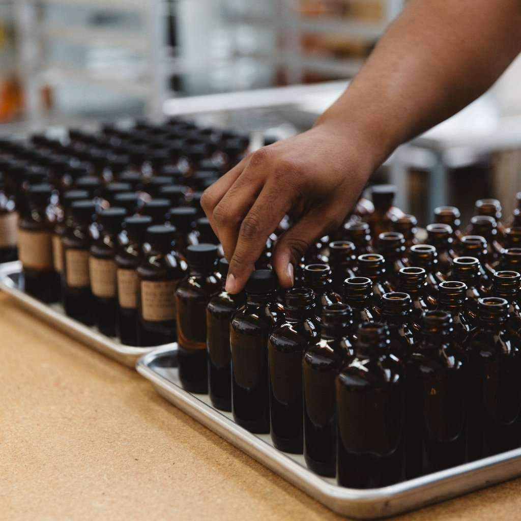 Person arranging brown glass bottles on a tray in a factory setting