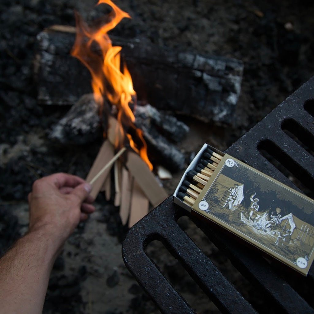 Person lighting a fire with a lit match near a campfire