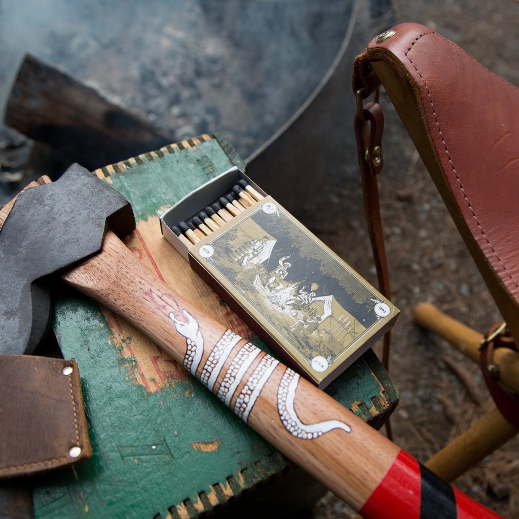 Matchbox with matches, ax, and leather pouch on a wooden surface