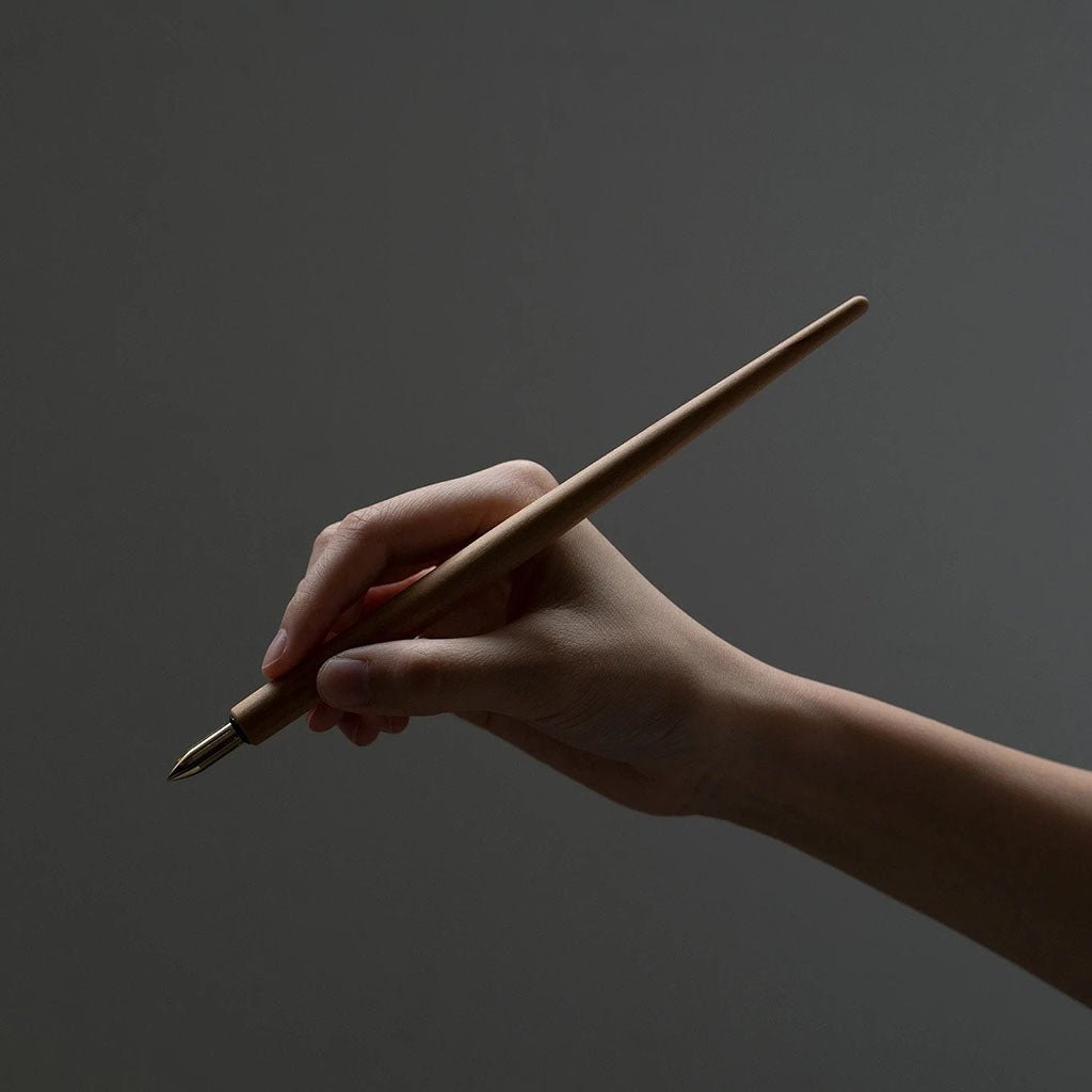 Hand holding a wooden dip pen against a dark background