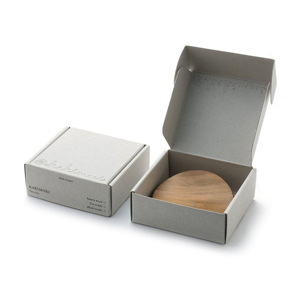 Wooden pen rest in an open box with a closed box next to it on a white background