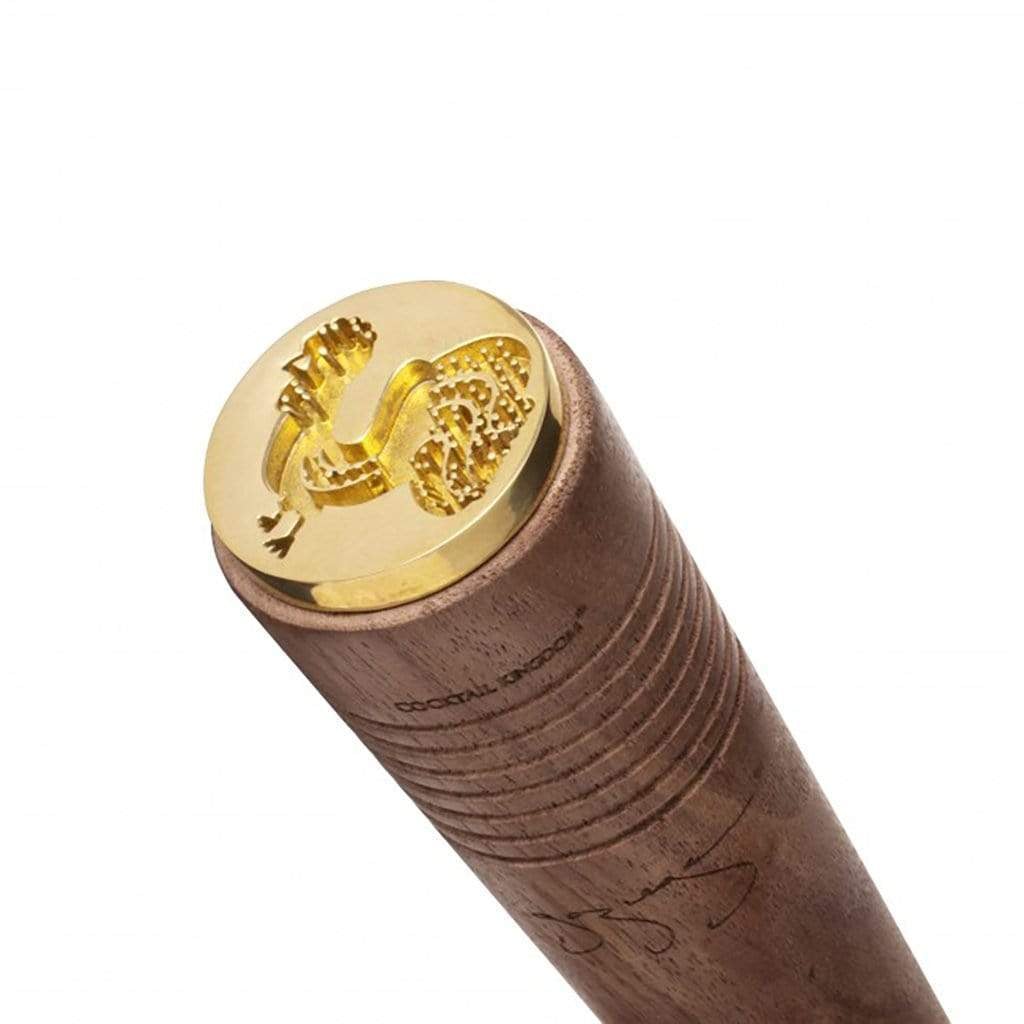 Brass rooster ice stamp on end of wooden muddler against white background