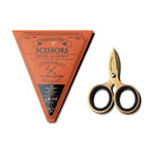 Pair of small three inch gold steel scissors next to orange triangular packaging with Tools to Liveby branding on white background