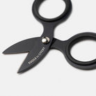 Close up of small black steel scissors with 'Tools to Liveby' branding on blade on white surface
