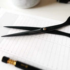 Black stainless steel scissors with 'TOOLS to LIVEBY' branding on blades laying on sheet of lined paper