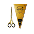 Gold-colored stainless steel scissors with black-rimmed finger loops, shown next to their yellow triangular branded packaging on a white background.