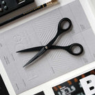 Black stainless steel scissors with 'TOOLS to LIVEBY' branding on blades on a gray sheet of paper.